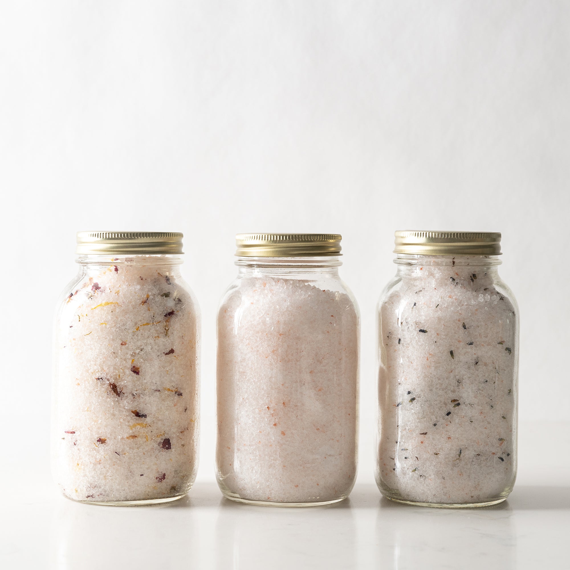 Three glass jars with gold lids containing a white powdery substance on a white background