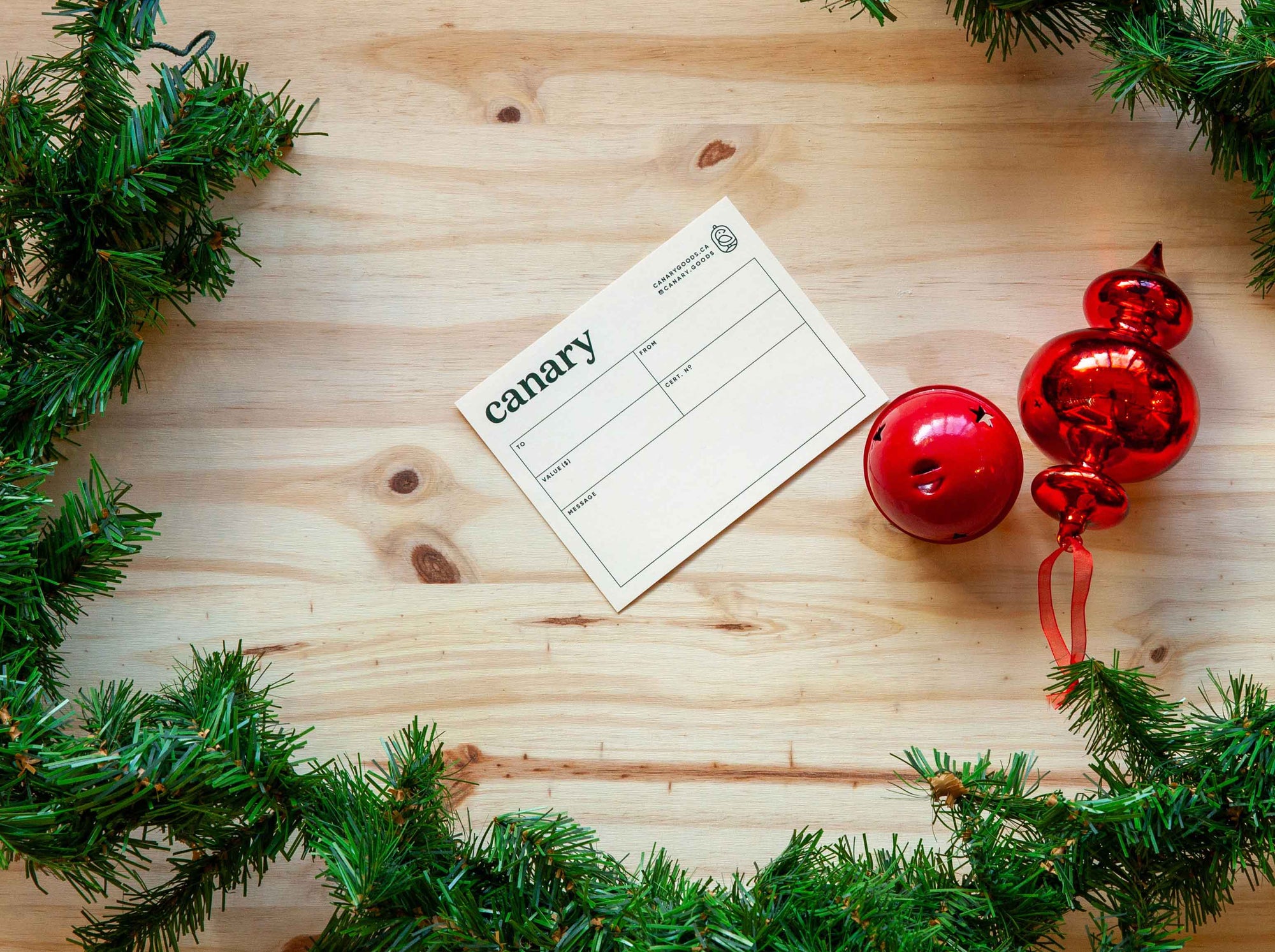A Canary gift card on a wood background with a Christmas ornament and wreath surrounding it. 