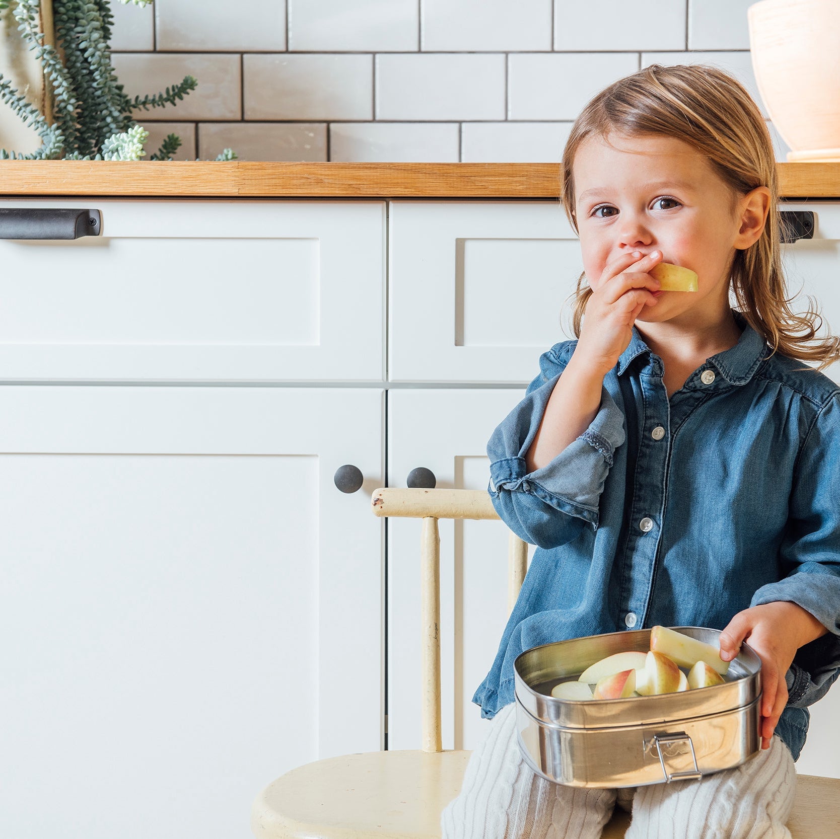 Child in a kitchen holding a bowl of food, eating from it.