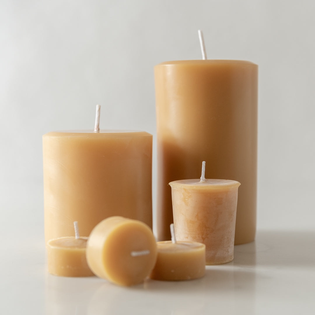 A group of beige beeswax candles of various sizes with cotton wicks, displayed on a light background.