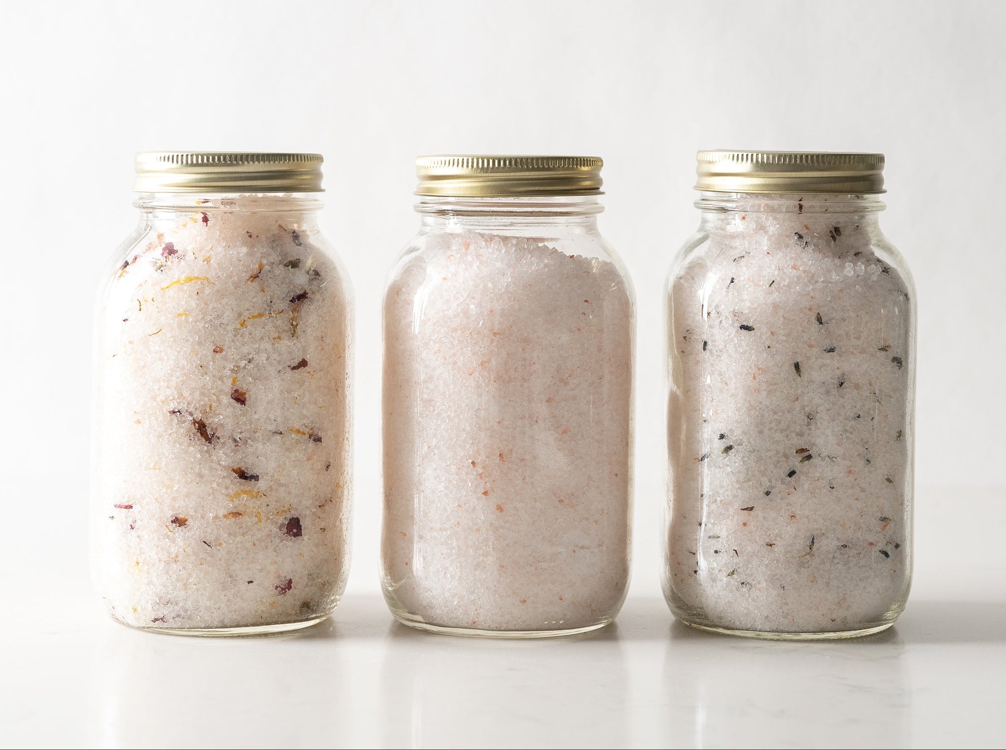 Three jars of bath salts with gold lids on a white background